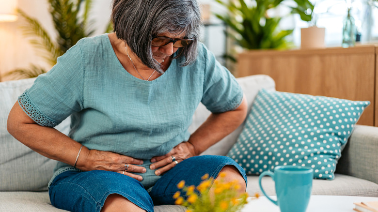 older woman holding onto stomach in pain on sofa