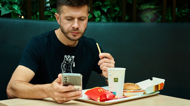 man eating McDonald's and checking out his phone