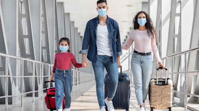 Masked family walking through airport with luggage