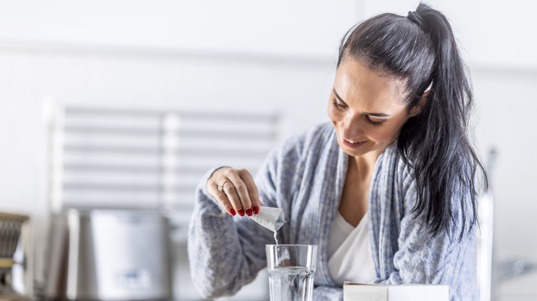 A woman's hand holding some supplement tablets and a glass of water