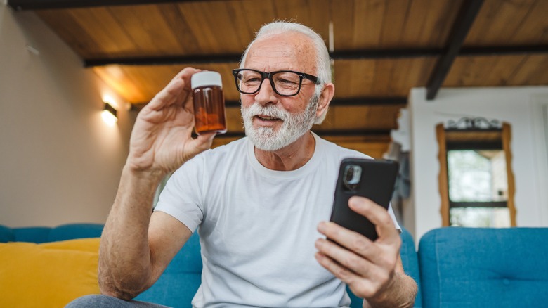 older man looking at supplement bottle while holding phone