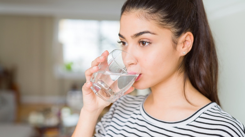Woman in black and white striped shirt holding glass of water up to her mouth