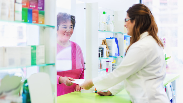 Older woman handing prescription to pharmacist