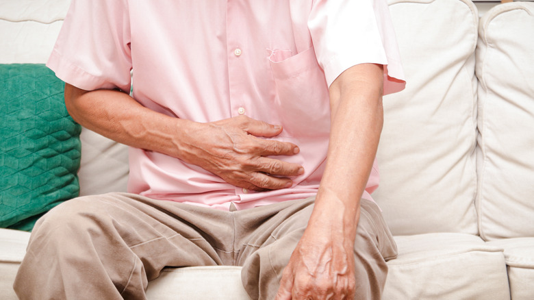 elderly man in pink shirt with hand on stomach in pain
