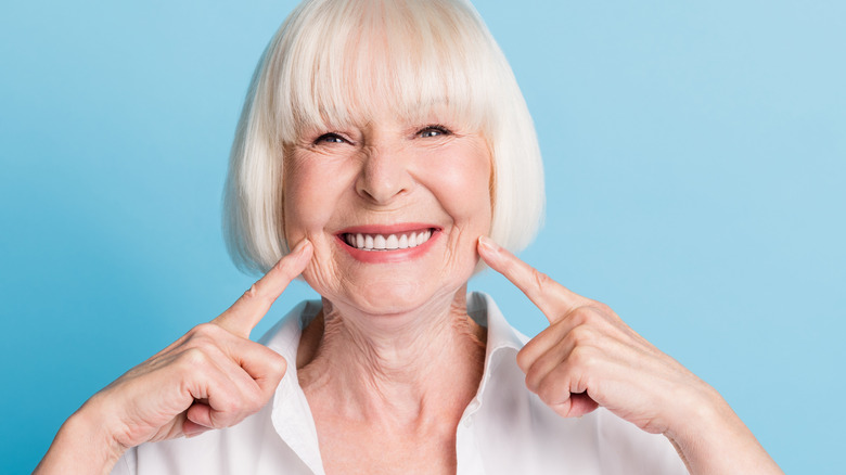 elderly female pointing with both hands at her healthy smile