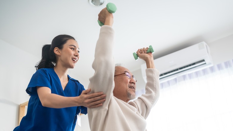 elderly male lifting light weights with support of a caregiver