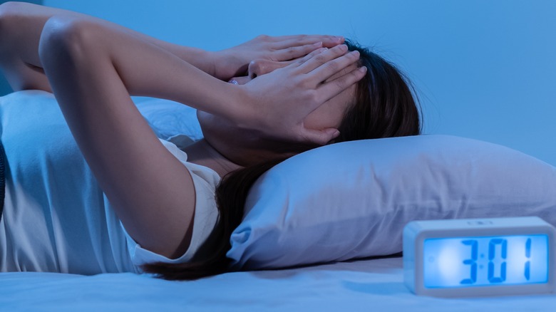 Young female laying in bed with hands on face. 