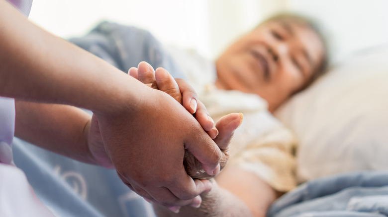 A nurse holds the hand of a woman in a nursing home