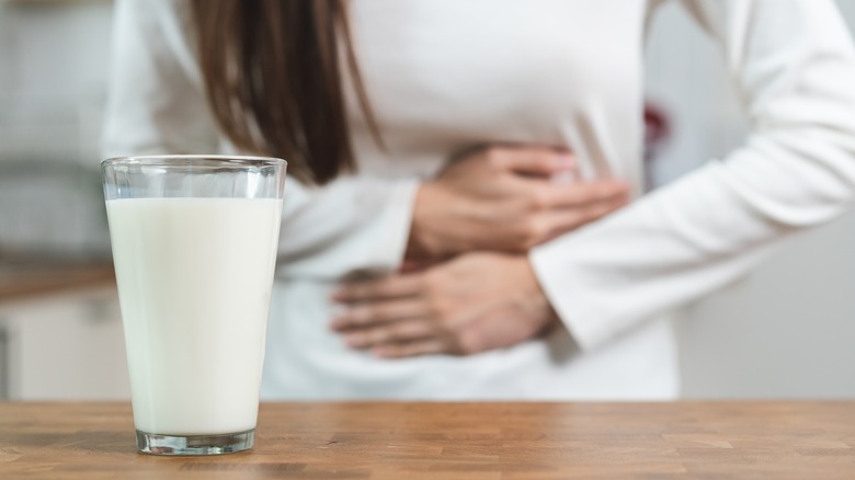 woman holding stomach behind glass of milk