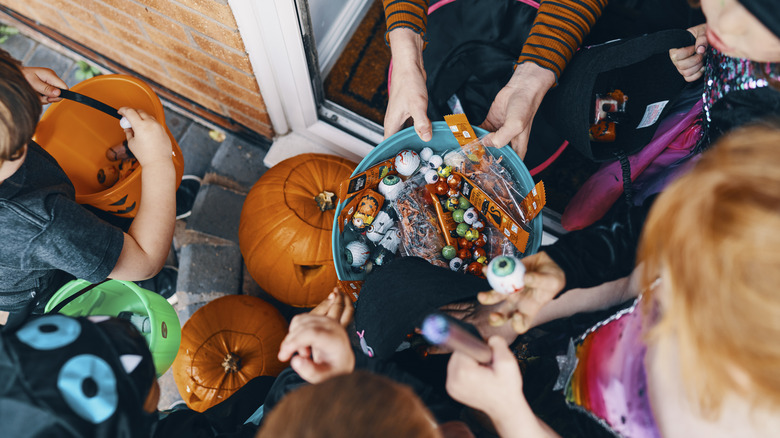 woman offering trick-or-treat items to costumed children