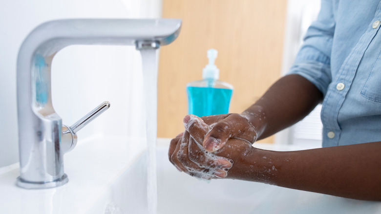 Pair of hands lathered in soap under running water in sink