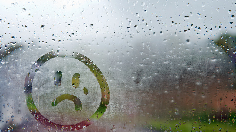 sad face drawn on rainy window 