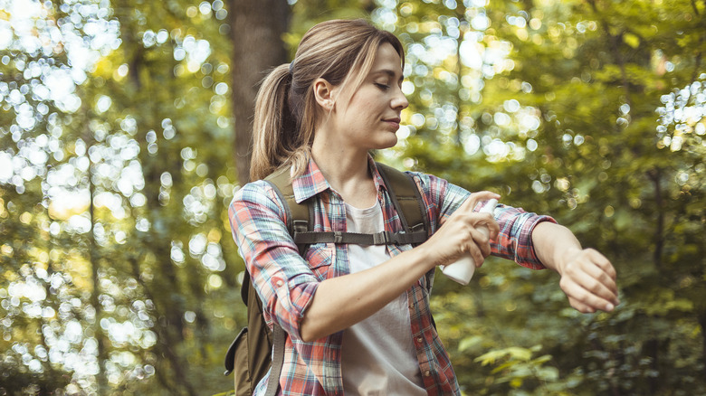 woman applying mosquito repellant while hiking in the woods