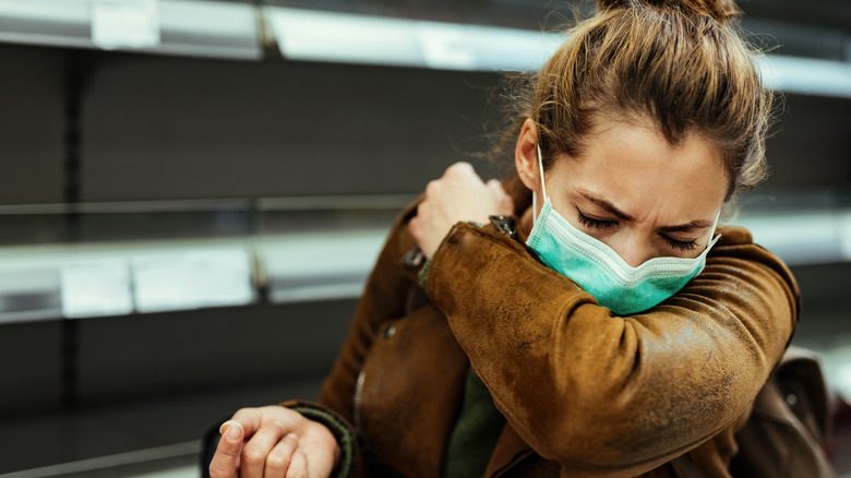 Masked woman coughing into sleeve