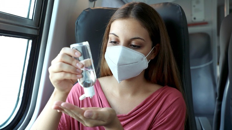 masked woman on airplane using hand sanitizer