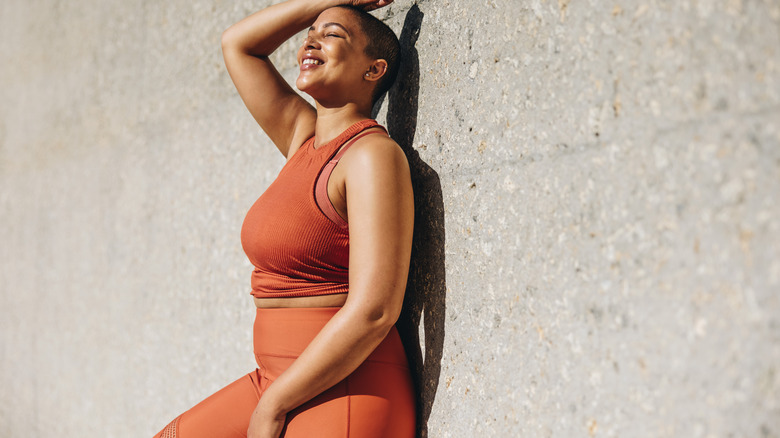 Black woman wearing workout gear leaning against a wall