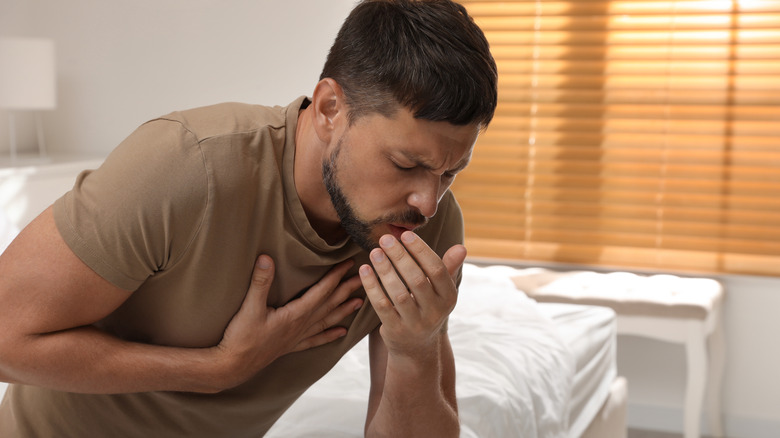 Seated man coughing on bed
