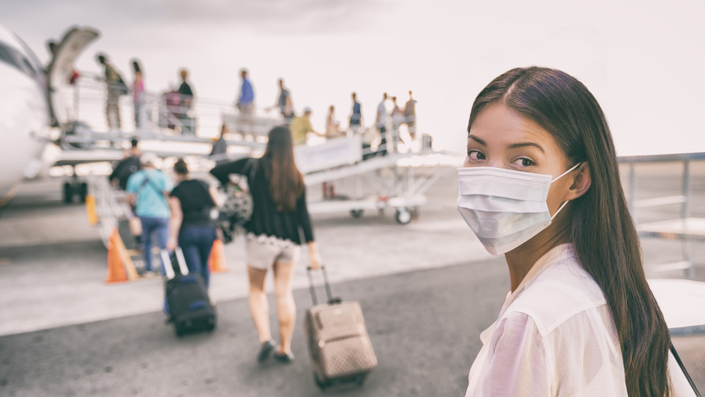 Young woman walking to a plane with a mask on 