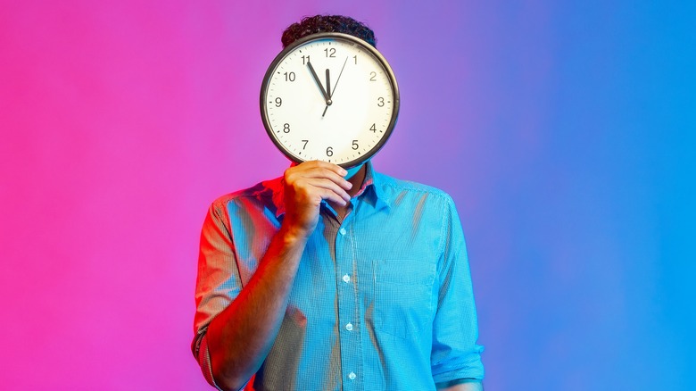 man holding large clock that covers his entire face