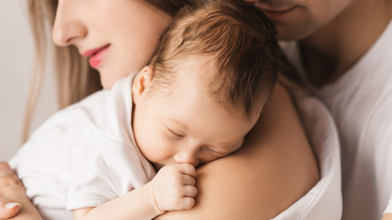 mother holding infant with dad hugging them from behind