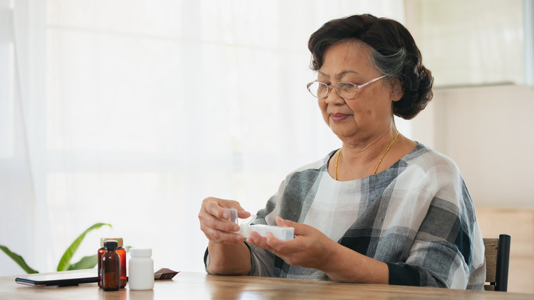 older Asian woman sitting at a table and opening a pill box