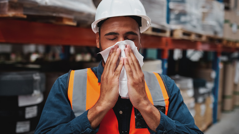 middle-aged, dark-skinned male worker blowing nose in warehouse