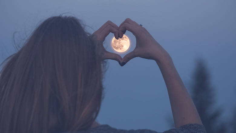 woman with hands in heart shape around moon