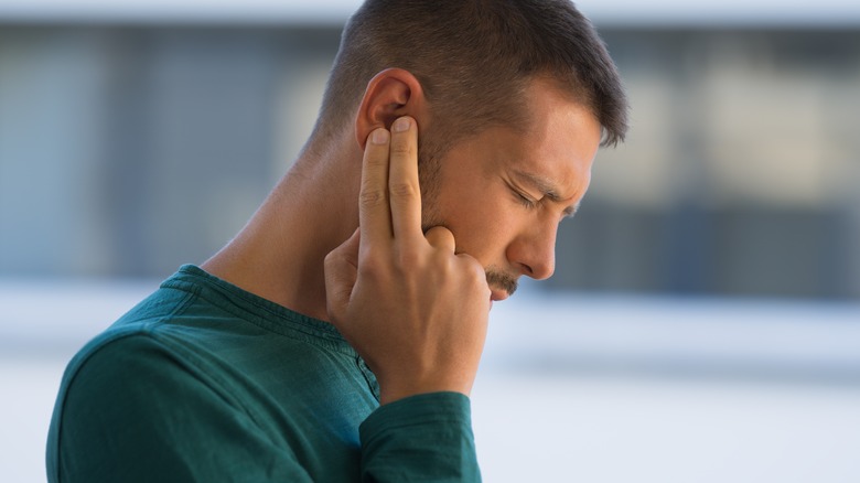 man touching ear with pained expression