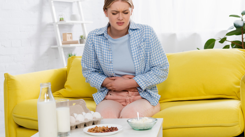woman clutches stomach in pain looking at dairy products and milk
