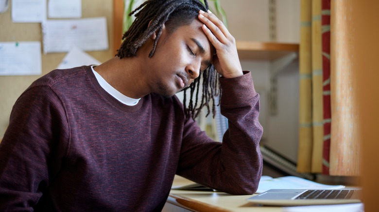 stressed man sitting at desk puts hand on forehead