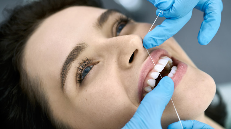 Person lying down having their teeth flossed by a dental hygienist with blue surgical gloves on 