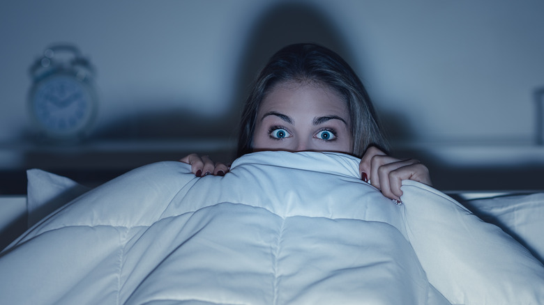 Woman watching tv in bed hiding under blanket