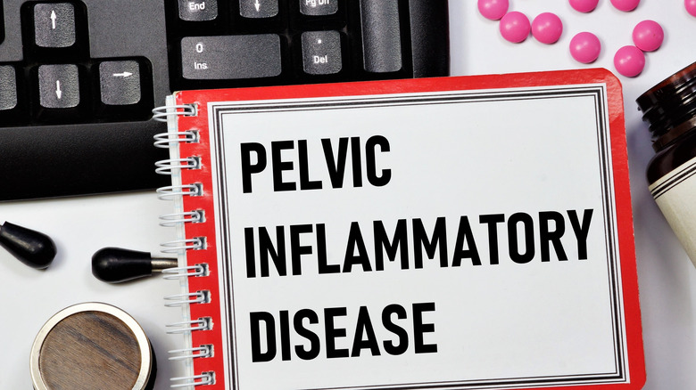 a notebook with the words pelvic inflammatory disease by a keyboard with pills