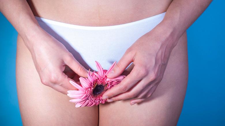 woman holding a flower over her groin
