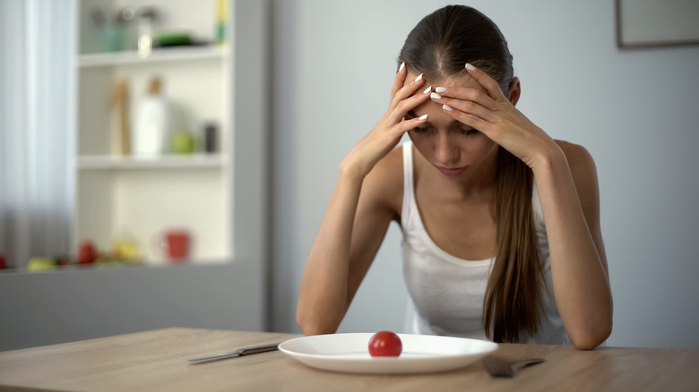 skinny woman looking down at plate with only a tomato