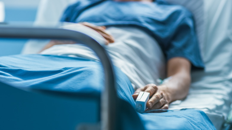 Person resting in hospital bed with pulse oximeter on finger