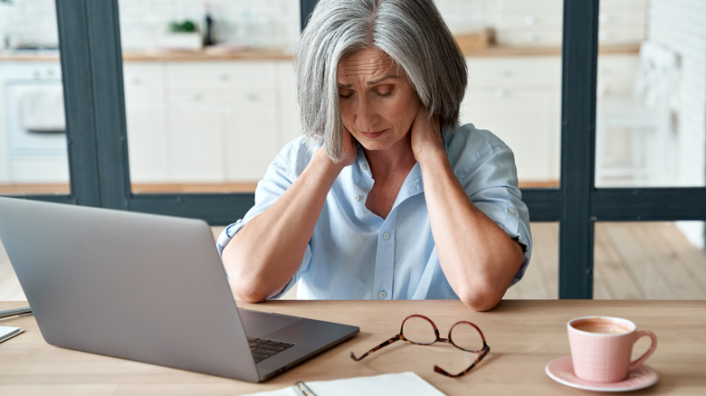 Mature woman sitting at her desk, feeling tired and sore