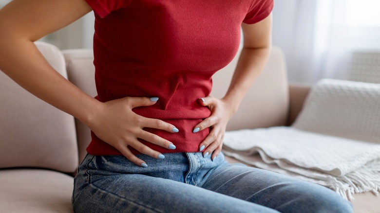 woman holding stomach while sitting on couch