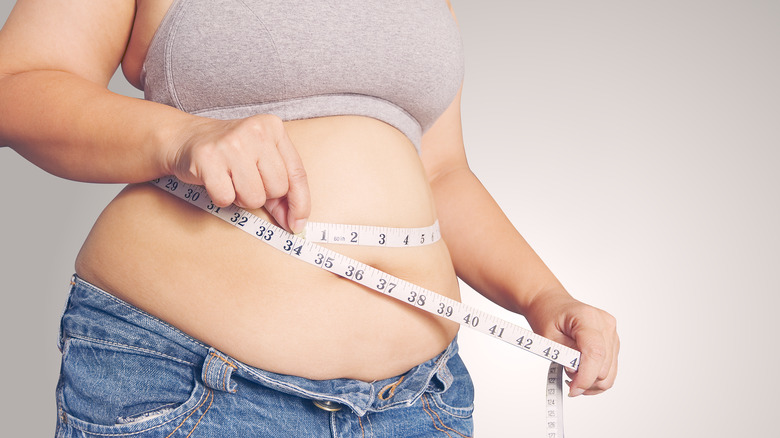 larger woman holding a measuring tape around her exposed belly 