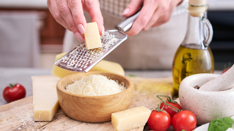 A woman's hand grating a block of Parmesan cheese