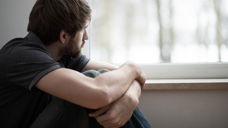 man sitting, sadly looking out window