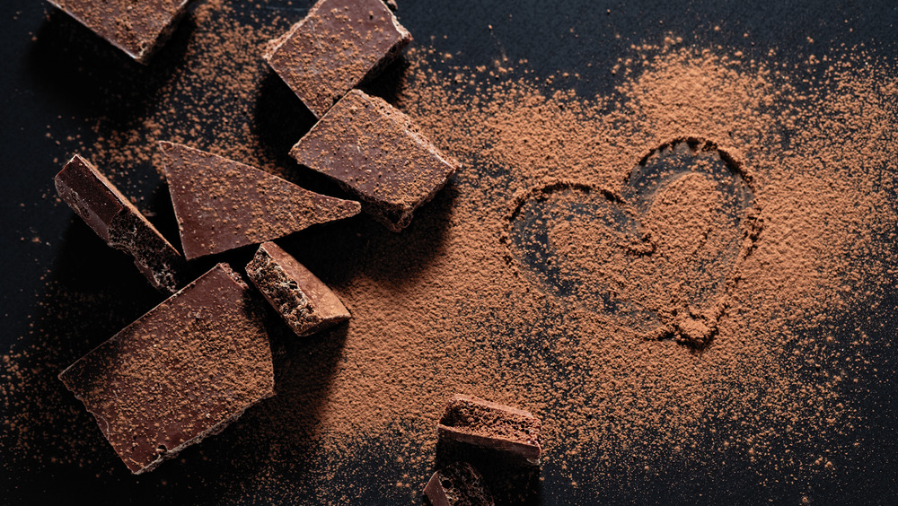 Broken pieces of chocolate with cocoa powder sprinkled on a surface and a heart drawn into the powder