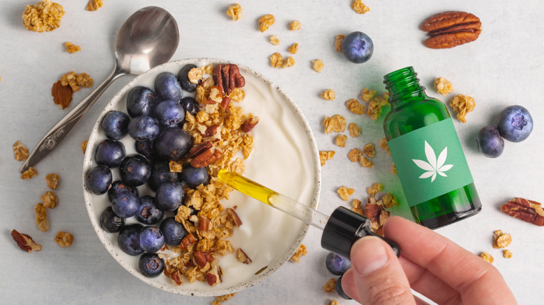 man squeezing cbd oil on yogurt bowl with blueberries and granola