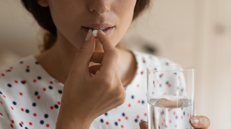 A woman about to take a pill and holding a glass of water