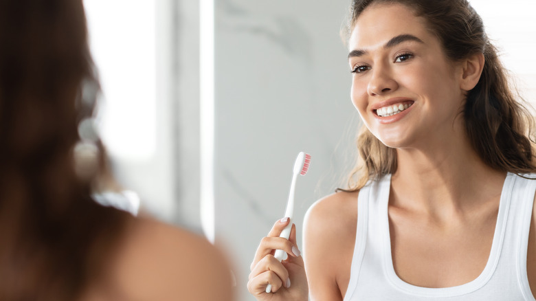 woman brushing teeth looking in mirror