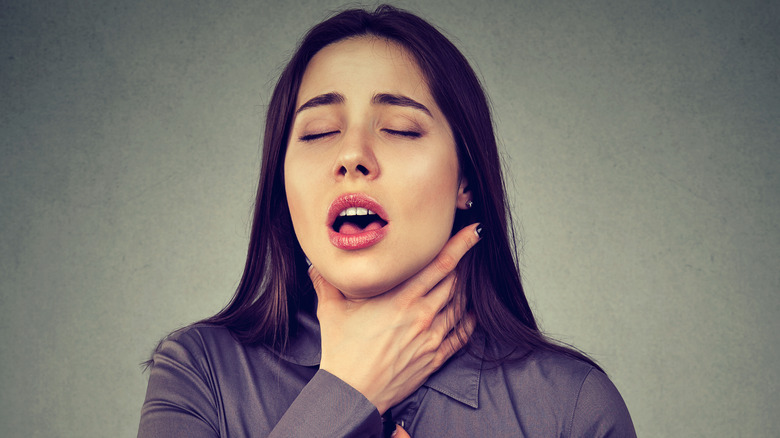 Woman holding throat on gray background