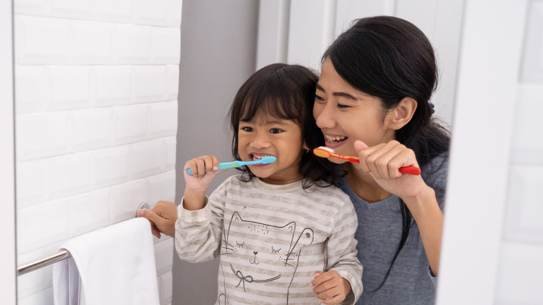 A mother and her daughter brush their teeth