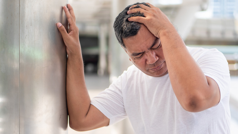 Man leaning on wall clutching his head feeling dizzy