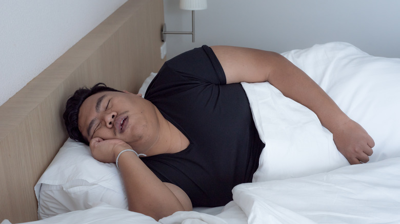 an overweight man snores in bed 