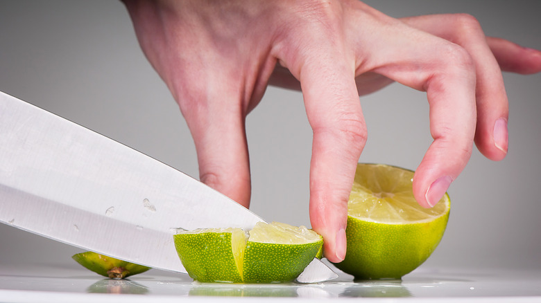 Close up of hand slicing limes on cutting board with knife
